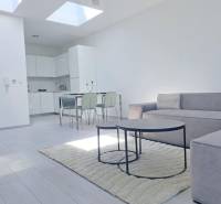 A bright living room with a kitchen, a sofa, and a wooden decor floor in a two-room apartment.