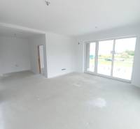 A bright living room in a two-room apartment with large windows and an empty floor.