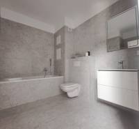 A bathroom with a bathtub, toilet, and sink in a 2-room apartment, the interior has light ceramic tiles.