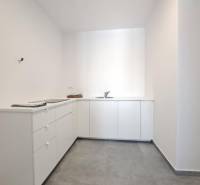 Kitchen area of commercial premises with white furniture and gray flooring.