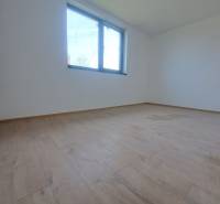 A spacious room with a wood-patterned floor and a large window in a family house.