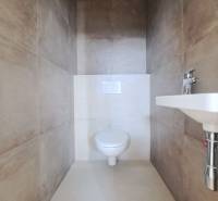 A toilet in a family house with beige ceramic tiles and a sink.