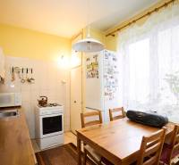A kitchen in a 3-room apartment with a wooden table, a stove, and white cabinets.