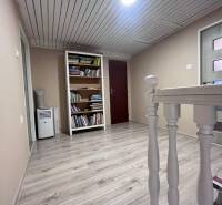 A hallway with a wood-patterned floor, a bookshelf, and light wooden railing in a family house.