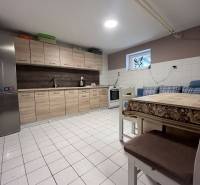 A kitchen in a family house with tiles, wooden cabinets, a refrigerator, and a dining table.
