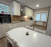 A kitchen in a family house with white furniture and a wooden decor floor.