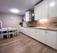 White kitchen with wood-patterned flooring in a family house. Dining table, wooden cabinets.