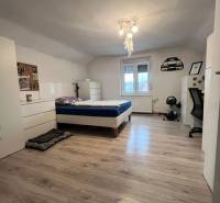 A bedroom in a family house with a bed, white furniture, and a floor with a wooden decor.