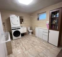 A bathroom in a family house with a washing machine, dryer, bathtub, and storage cabinets.