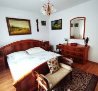 A bedroom in a family house with wooden furniture, a floor with a wooden decor, and paintings on the wall.
