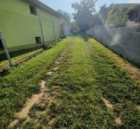 Plots - housing in Veľké Zálužie with a grassy path between the fence and the wall.