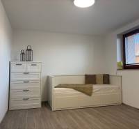 A room in a family house with a bed, a dresser, and a wooden-patterned floor.