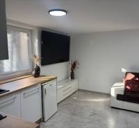 Living room in a family house with a white kitchen unit and a dark brown sofa.