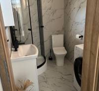 A bathroom in a family house with marble tiling, a shower cabin, and a washing machine.