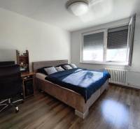 A bedroom with wood-patterned flooring, a desk, and a bed in a studio apartment.