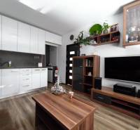 A kitchenette with white cabinets, a television, furniture, and a wooden decor floor in a studio apartment.