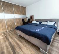 A bedroom in a studio apartment with a wood-patterned floor and built-in wardrobes.