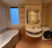 A bathroom in a 3-room apartment with a bathtub, sink, washing machine, and tiles.