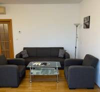 Gray sofa in a 3-room apartment with wood-patterned flooring and a glass table.