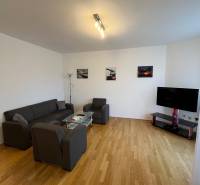 Living room in a three-room apartment with a wooden decor floor, a sofa, and a television.