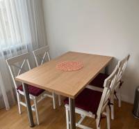 A dining table with four chairs and a wooden decor floor in a three-room apartment.