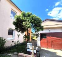 A family house in Partizánske with a garage, a green tree, and a well-fenced garden.