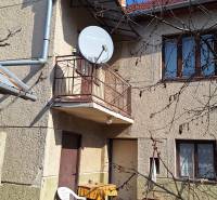A family house in Tachtá with a balcony, satellite dish, and garden chairs under the blue sky.