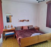 Bedroom in a family house with textile curtains, patterned carpet, and a bed.