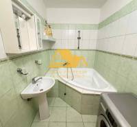 A bathroom in a 3-room apartment with a corner bathtub, sink, and washing machine.