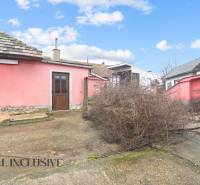A family house in Šintava with a pink facade, an unkempt yard, and wooden doors.