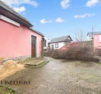 The exterior of a family house in Šintava with a pink facade, yard, and shrubs.