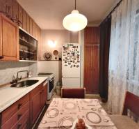 A kitchen in a 3-room apartment with wooden cabinets and a refrigerator, decorated with curtains.