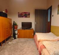 A room in a 3-room apartment with a carpeted floor, a bed, and wooden furniture.