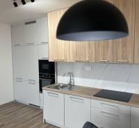 A kitchen in a two-room apartment with a wooden decor floor and light furniture.