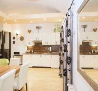 The kitchen of a 2-room apartment with a wooden decor floor, white cabinets, and a table.