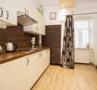 A kitchen with a wood-patterned floor in a 2-room apartment, white cabinets, and patterned curtains.