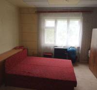 A bedroom in a family house with simple furniture and a red bed.