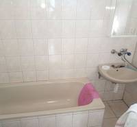 A bathroom with a bathtub and a sink in a family house, with light tiles and flooring.