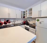 A kitchen in a 2-room apartment with light cabinets and red kitchen utensils.