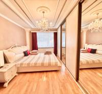 A bedroom with a chandelier, a large bed, and a floor with a wooden decor in a two-room apartment.