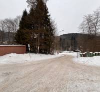 A snowy road in Oščadnica surrounded by trees and trash bins.