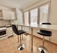 A kitchen in a 2-room apartment with a bar table, chairs, and white kitchen cabinets.