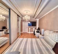 Bedroom in a two-room apartment with wood-patterned flooring and a large mirrored wardrobe.