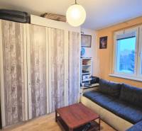 Studio apartment with wood-patterned flooring, a couch, cabinets, and a table. Minimalist interior.