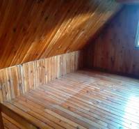 Attic in a cabin with wooden paneling and a floor with a wooden decor.