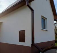 A cottage in Pozdišovce with a white facade and a dark gutter system.