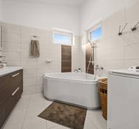 A bathroom in a family house with a bathtub, washing machine, brown and white tiles, and a cabinet.