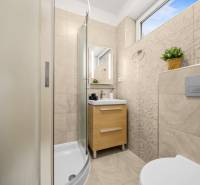 A bathroom in a family house with a shower, a sink, and light-colored tiles.