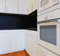 A kitchen in a 2-room apartment with white cabinets, a black countertop, and a wooden-patterned floor.