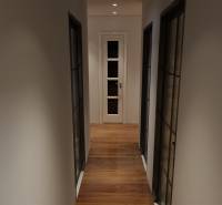 A hallway with a wooden decor floor and glass doors in a 3-room apartment.
